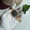 Rose gold watch held by a gloved hand with a blurred background