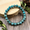 Side Angle View Of Blue Green Turquoise Mineral Bead Bracelet Resting Next To Fresh Green Leaves On Light Wooden Texture